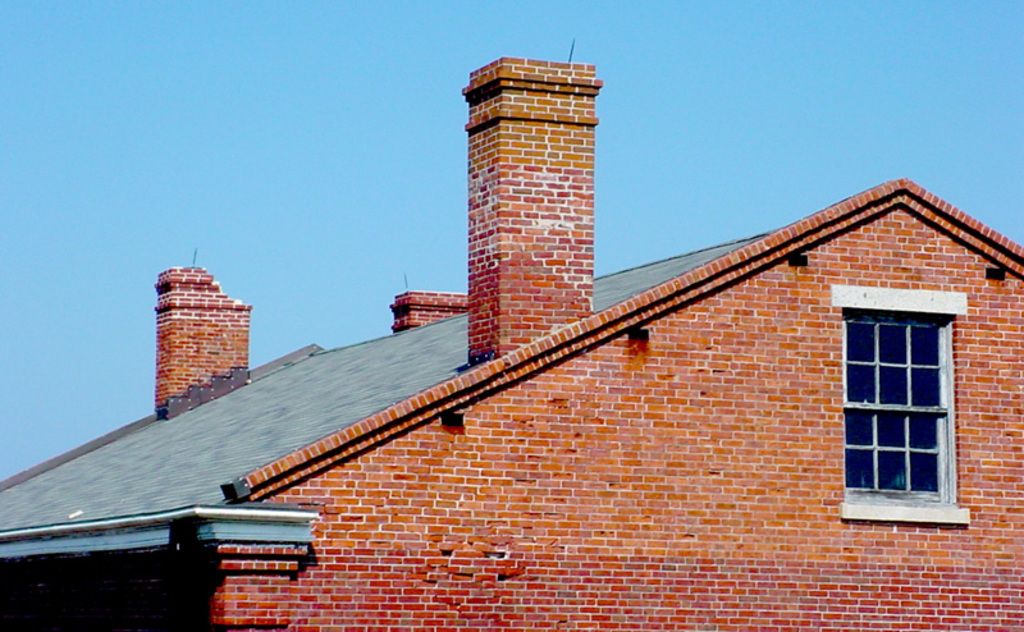 Red brick house with a slate roof and tall chimneys under a clear blue sky